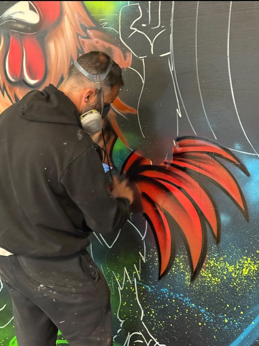 Artist spray painting the weightlifting chicken mural